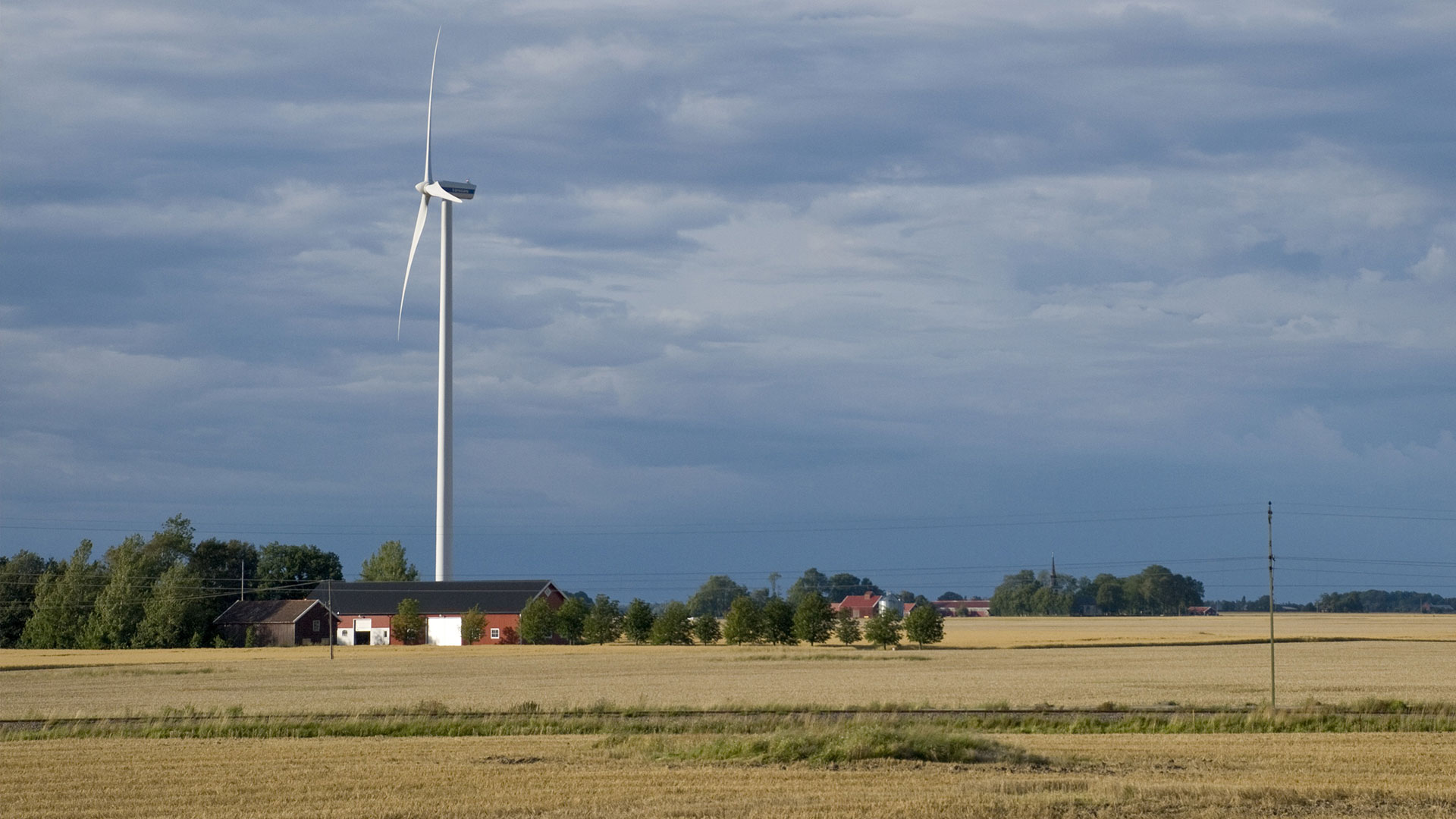 Vindkraftverk över en gård och åkrar.