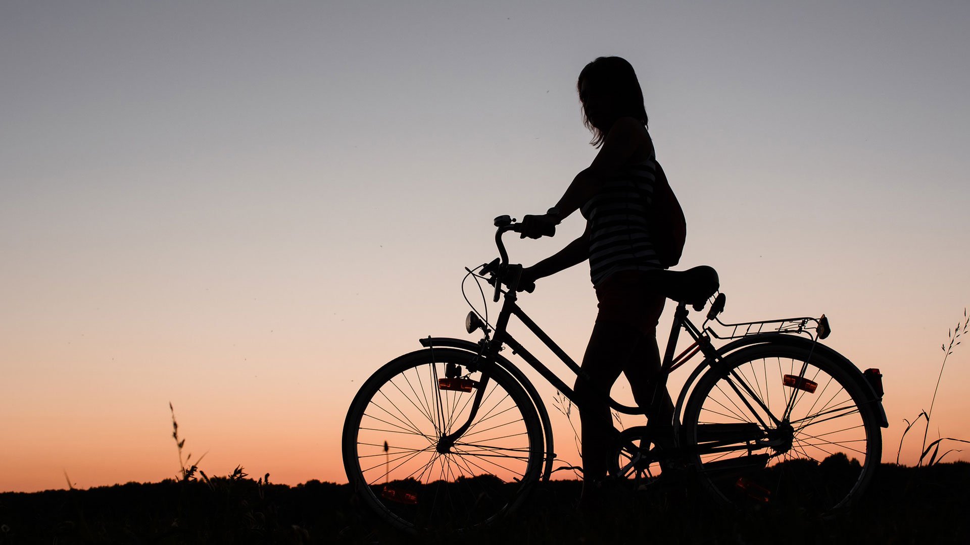 Siluett av en kvinna med cykel mot solnedgång.